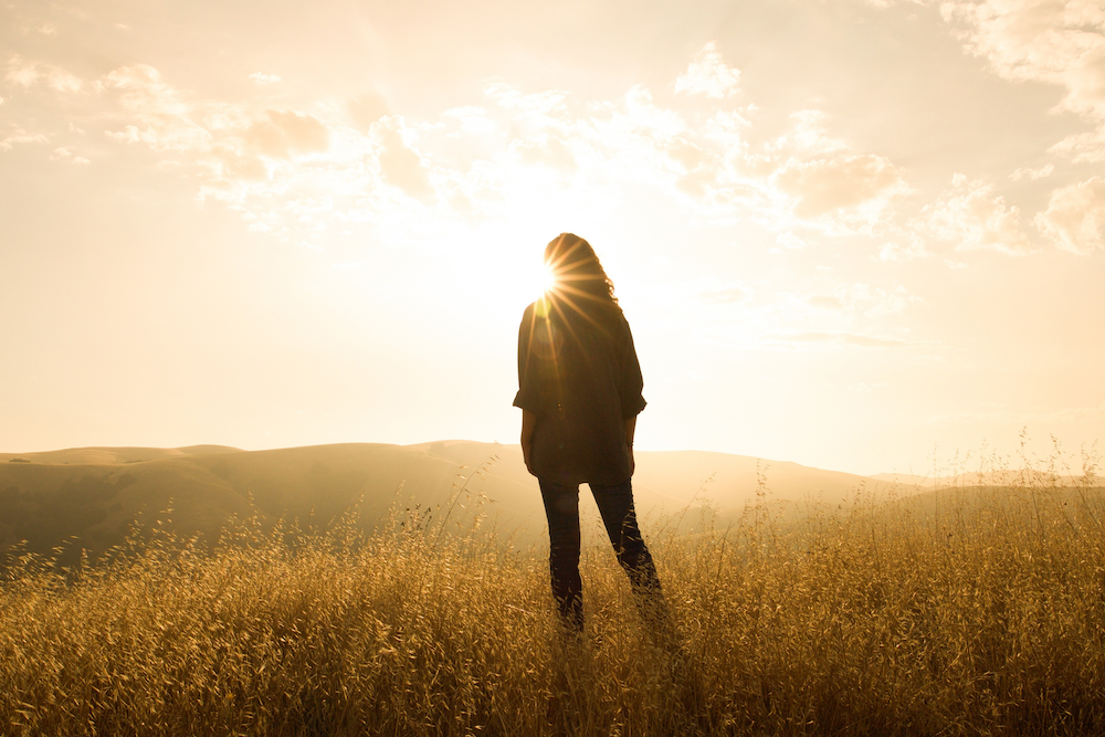 Woman standing alone in a golden field at sunset